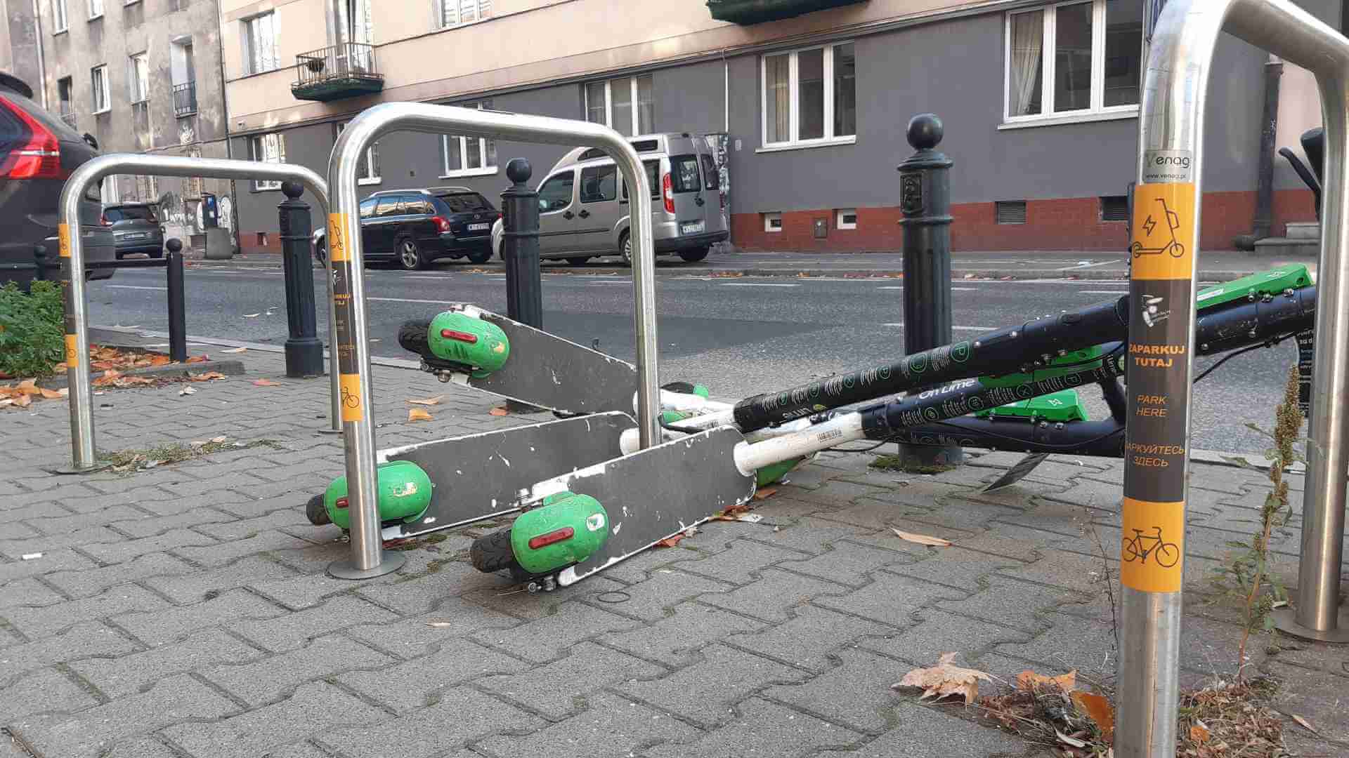 Hulajnogi elektryczne przewrócone przy stojakach rowerowych