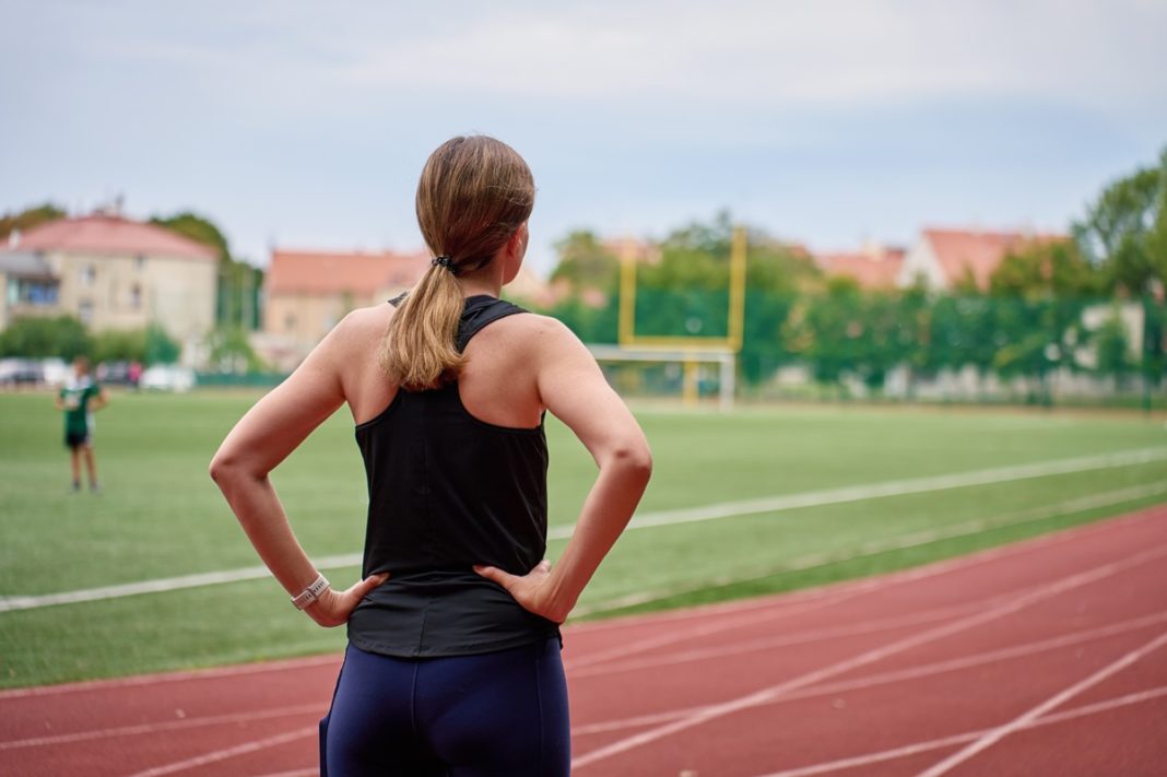 Woman standing with hands on hips by running track before workout Smartwatch z pomiarami parametrów organizmu to akcesorium często wybierane przez sportowców